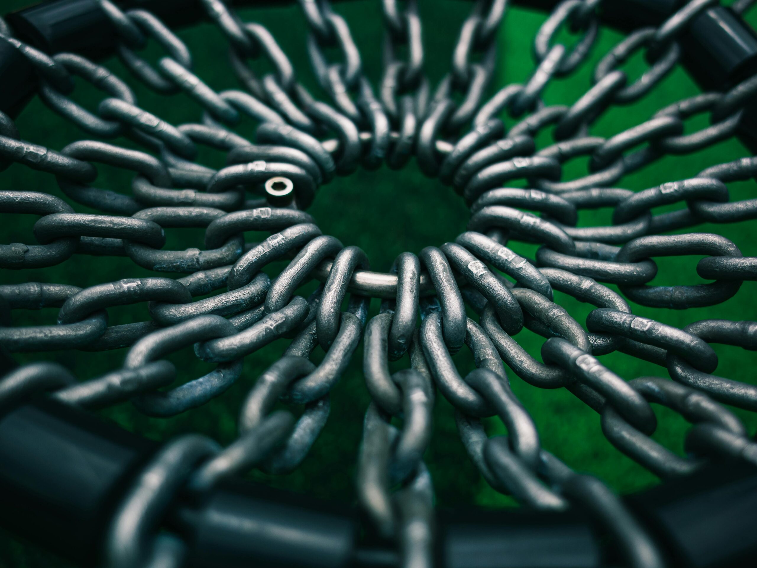 Top view of interwoven metal chains forming a circle against a green backdrop, creating a striking industrial pattern.